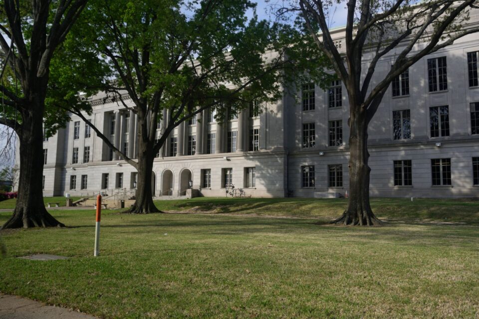 A historic building facade framed by mature trees and a green lawn, evoking historic Bryan, TX