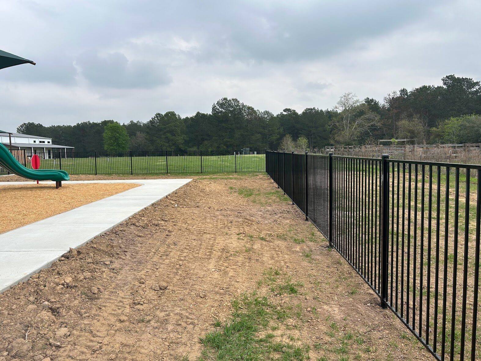 Bare soil along the fence line at a Tomball church playground before artificial turf installation
