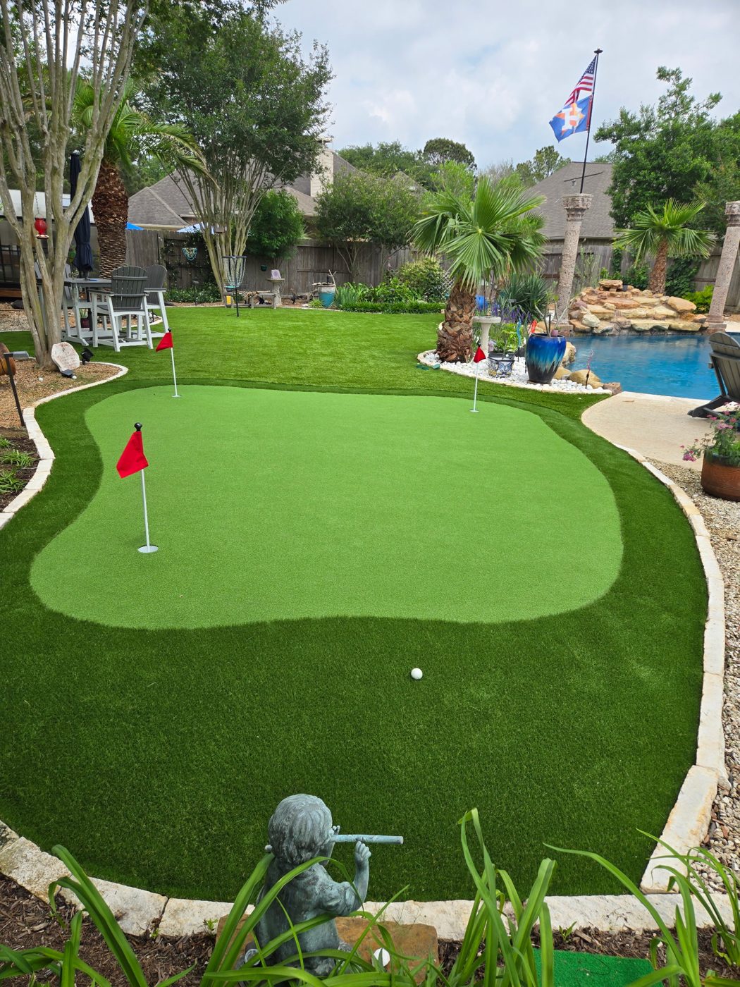 Backyard putting green with three flags next to a pool in Fulshear, TX
